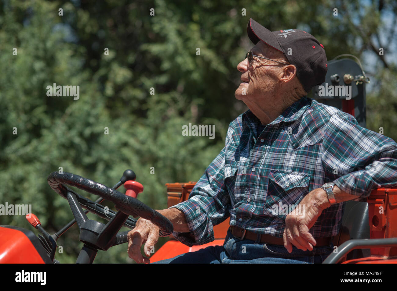 Un sincero ritratto di un senior, maschio agricoltore seduto su un trattore. Foto Stock