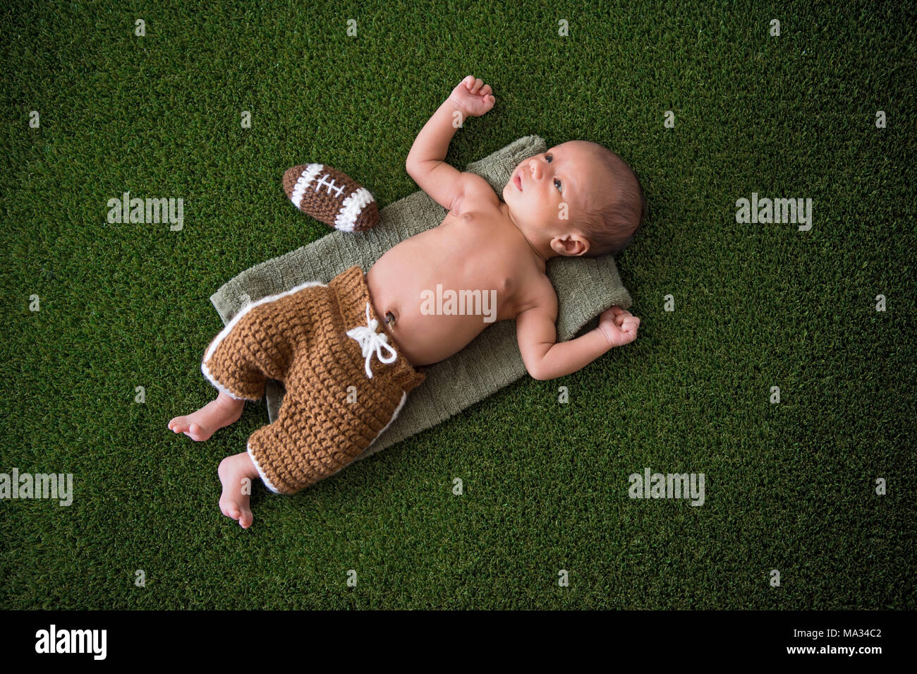 A due settimane di età, alert, Neonato Bimbo giacente sul tappeto erboso di erba con una maglia di football americano. Foto Stock