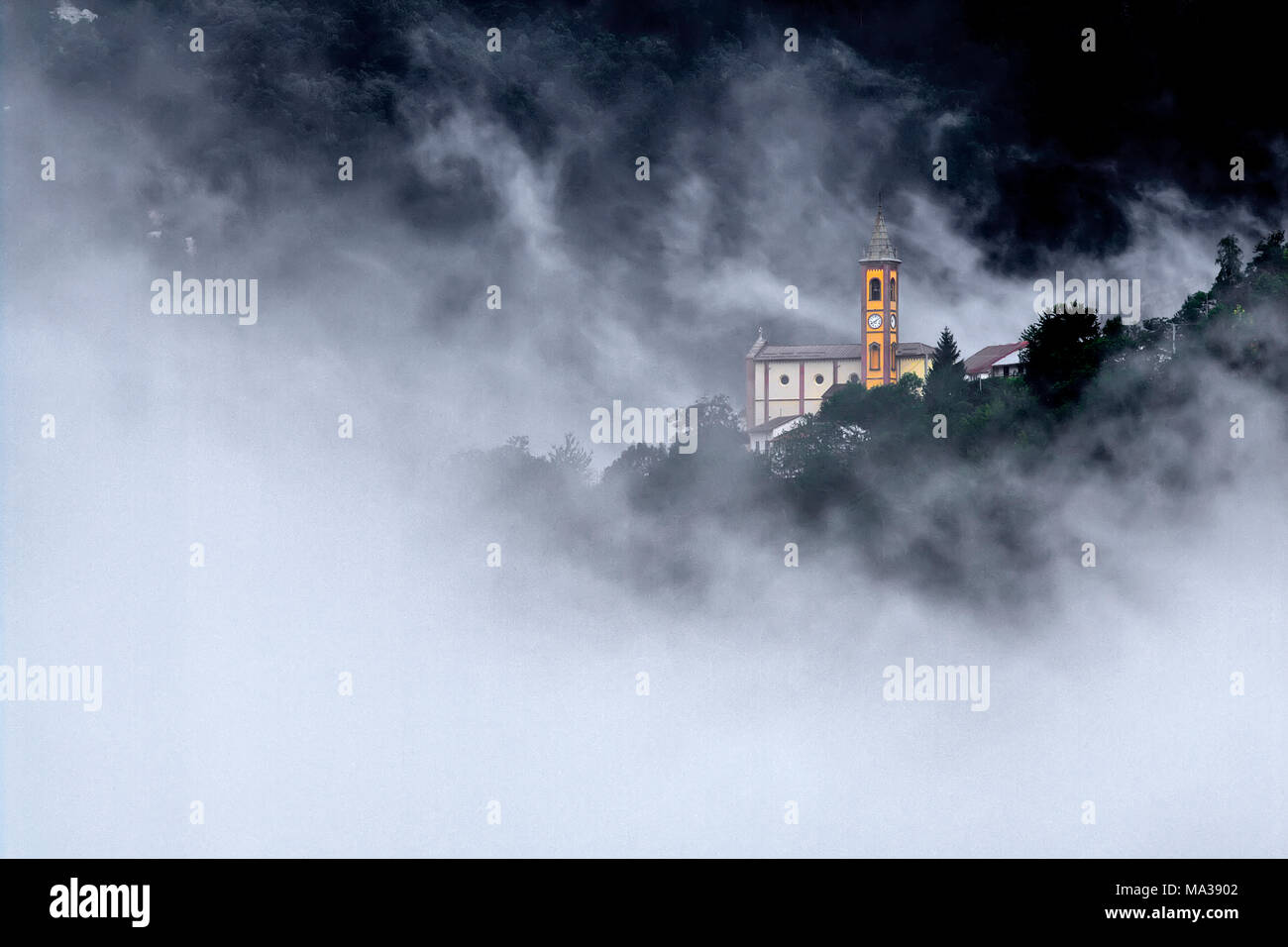 La chiesa del villaggio di cappello, comune di Garessio, in Alta Valle Tanaro, circondato dalla nebbia che risale la valle. Foto Stock