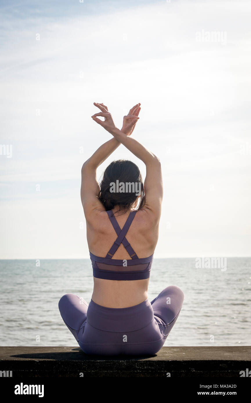 Vista posteriore di una donna pratica lo yoga e la meditazione seduta su una parete in riva al mare Foto Stock