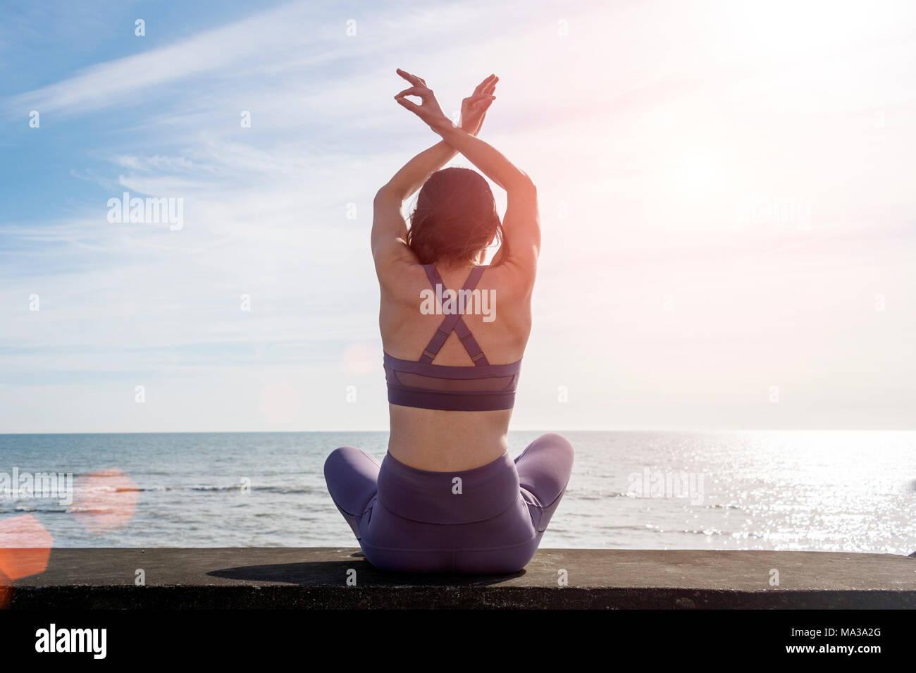 Vista posteriore di una donna pratica lo yoga e la meditazione seduta su una parete in riva al mare Foto Stock
