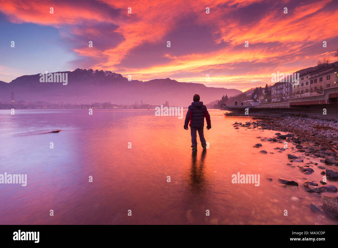 Uomo in acqua ammirare un incendio sunrise a Lecco e montagne, il lago di Como, Lombardia, Italia, Europa Foto Stock
