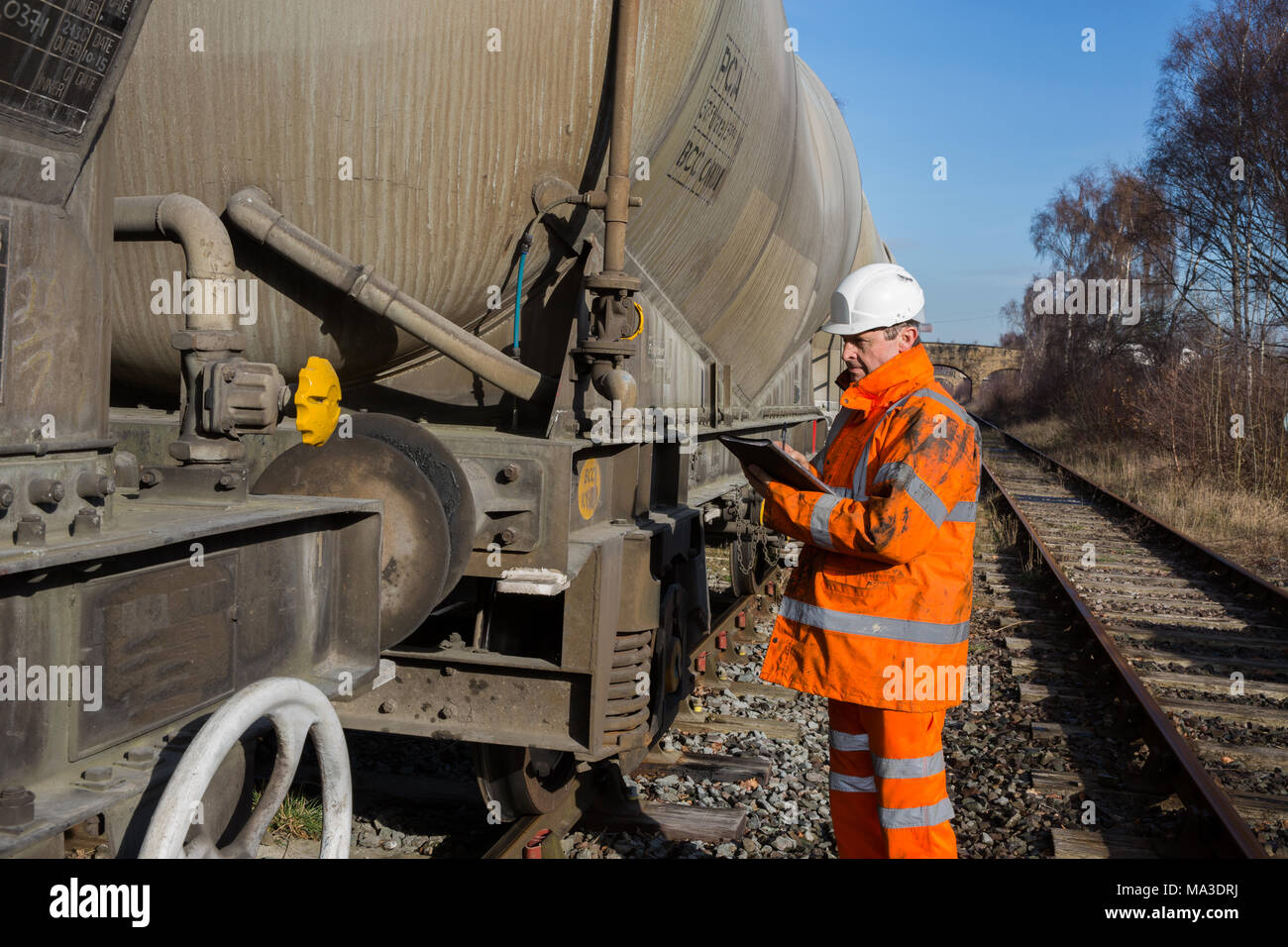 Un operaio ferroviario ad alta visibilità abbigliamento ispezionando un carro ferroviario durante una manutenzione periodica ispezione. Foto Stock