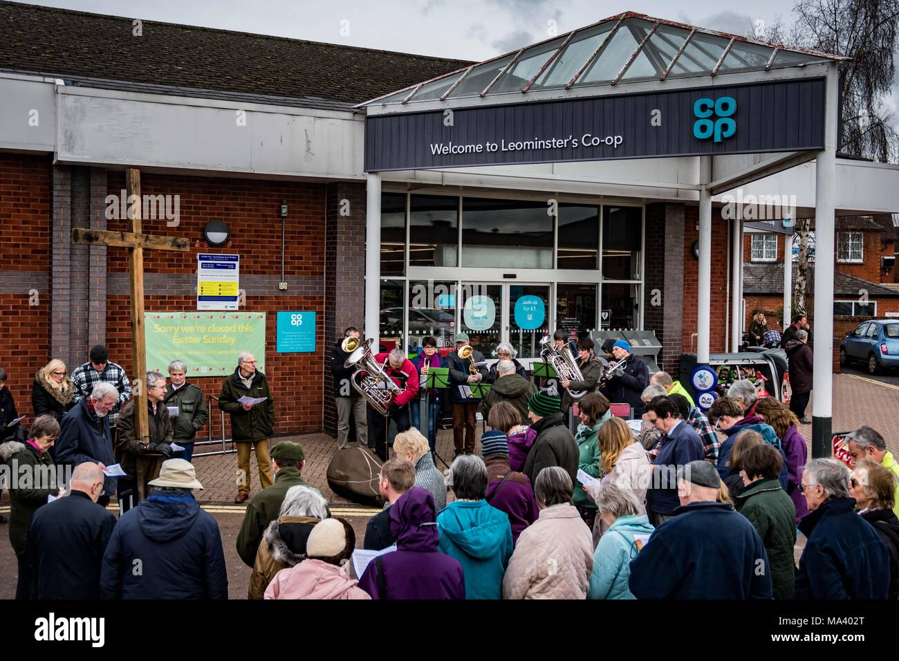 LEOMINSTER, Herefordshire, Regno Unito - 30 Marzo: i membri della comunità cristiana al di fuori di Co-op supermercato in Leominster si riuniscono per prendere parte a una processione del Venerdì santo come parte della settimana santa il 30 marzo 2018. Durante il cammino di testimonianza che essi portano la croce simbolica dalla Chiesa Battista Etnam Street attraverso il mercato medievale piazza del Priorato Chiesa su Church Street dove la Croce sarà eretta. Molte città e villaggi già tenere passeggiate o marche di testimonianza di vita come un segno del loro comune fede nella morte e risurrezione di Gesù Cristo. La vacanza cristiana commemora la CRU Foto Stock