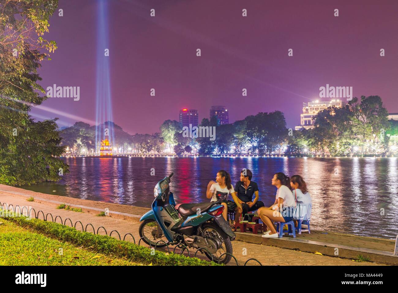 I giovani seduti accanto al lago Hoan Kiem ad Hanoi, Vietnam Foto Stock