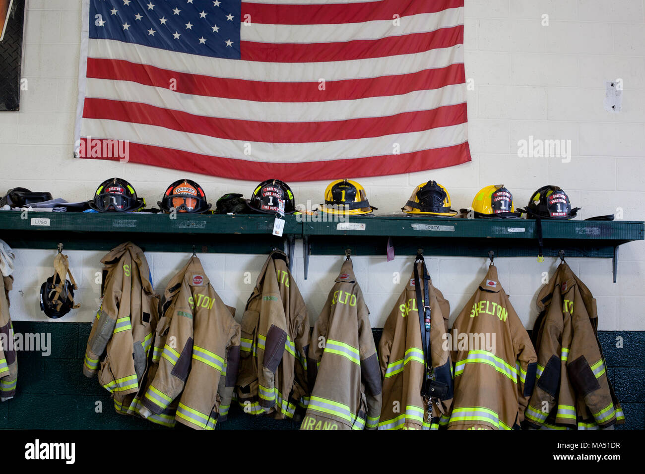 Indumenti di protezione, caschi per vigili del fuoco e affluenza cappotti lungo con una bandiera americana sul display nel volontariato locale firehouse Foto Stock