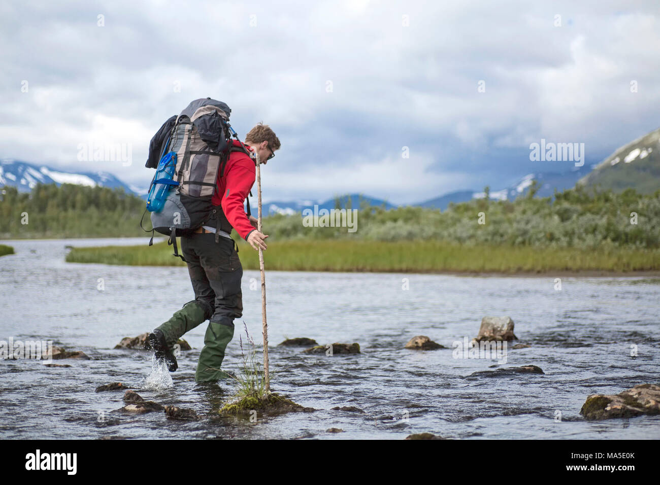 Escursionista che attraversa un fiume in Sarek National Park, Svezia Foto Stock