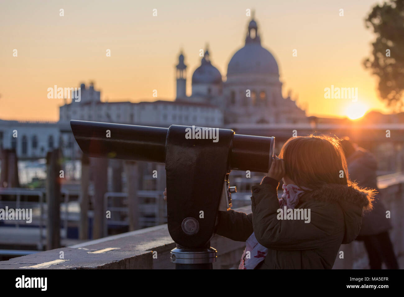 Bambina guardando attraverso il telescopio del Canal Grande e sullo sfondo la basilica di Santa Maria della Salute, Santa Maria della Salute al tramonto, Venezia, Veneto, Italia Foto Stock