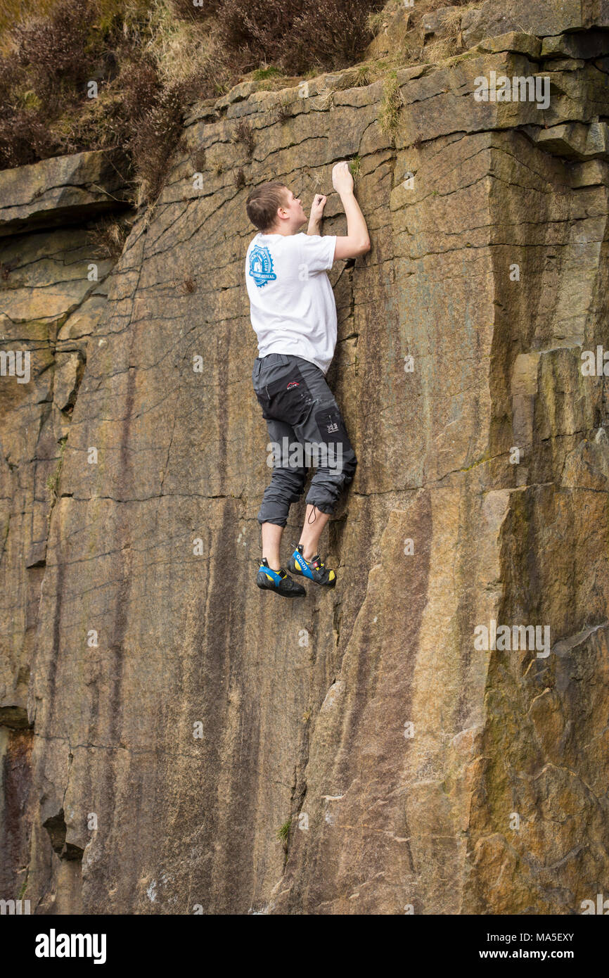 Giovane uomo rock climbing (bouldering) senza corde sulla roccia brunastro. Foto Stock