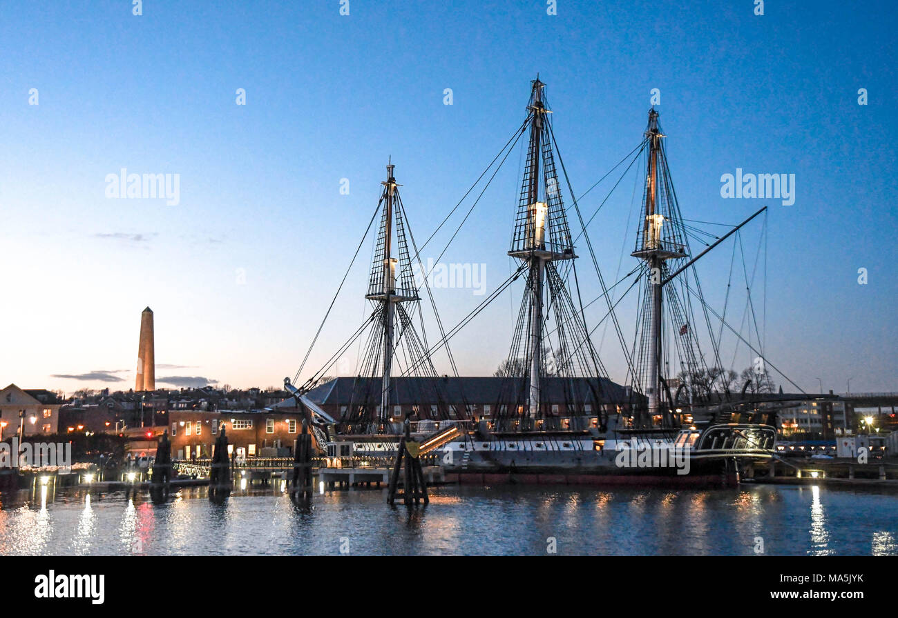 Il Museo della Portaerei U.S.S. Costituzione, che ha combattuto nella Rivoluzione Americana, ormeggiata nel porto di Boston con il Monumento di Bunker Hill in background al tramonto. Foto Stock