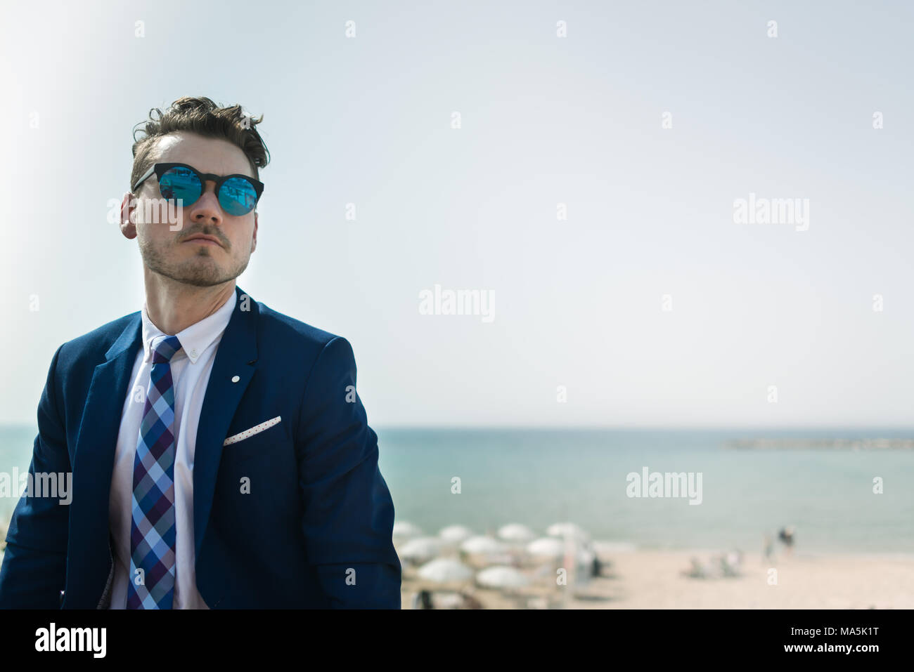 Giovane uomo gravi in elegante abito e sunglass sullo sfondo del mare e del cielo. Manager di successo è di relax all'aperto nella giornata di sole. Ragazzo alla moda Foto Stock