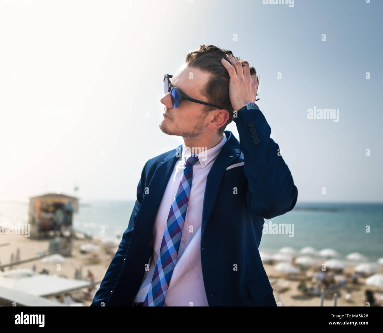 Giovane uomo corregge capelli su sfondo del mare e del cielo. Imprenditore di successo in tuta e sunglass è rilassante all'aperto nella giornata di sole. Ragazzo alla moda Foto Stock