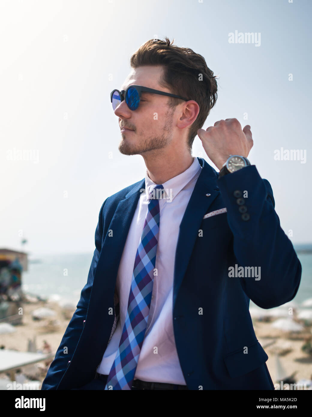 Giovane uomo elegante in abito elegante e sunglass sullo sfondo del mare e del cielo. Ragazzo di successo è rilassante all'aperto nel giorno caldo e soleggiato. Ragazzo alla moda Foto Stock