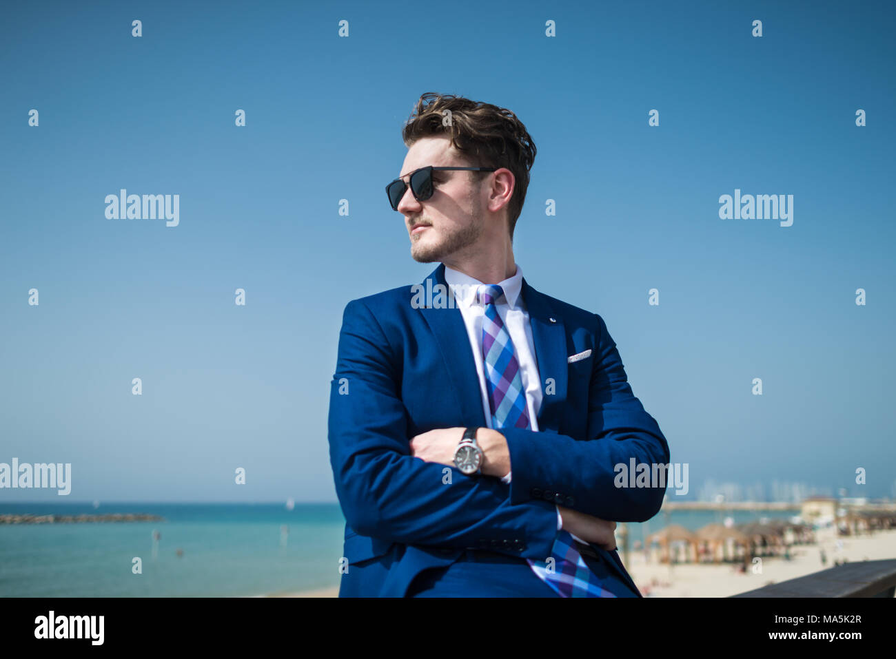 Giovane uomo gravi in elegante abito e sunglass sullo sfondo del mare e del cielo. Manager di successo all'aperto rilassante nel giorno caldo e soleggiato. Ragazzo alla moda Foto Stock