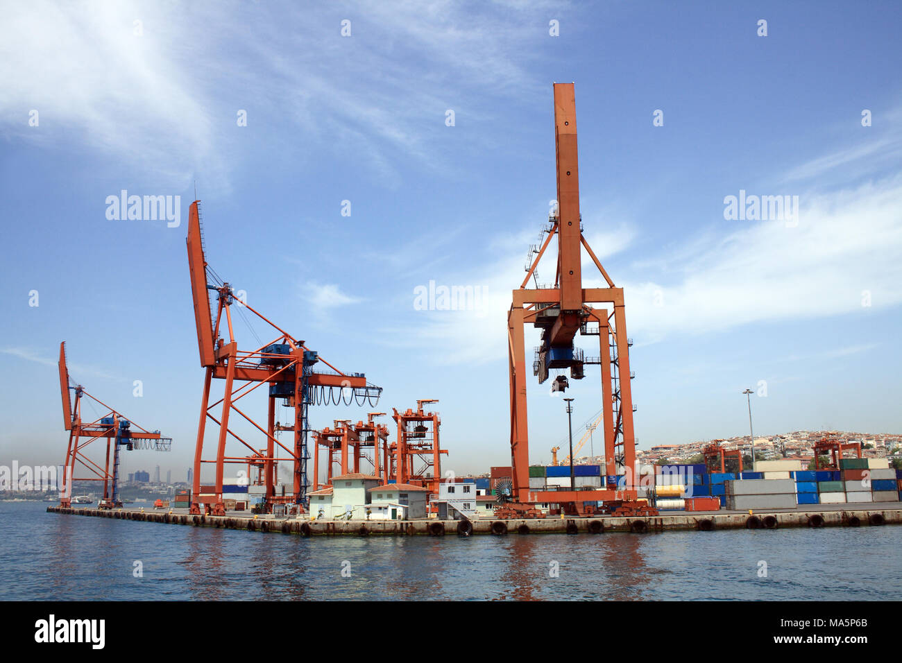 Panorama con cielo blu, il mare e il porto di contenitore. Primo piano di alcune gru rosso Foto Stock
