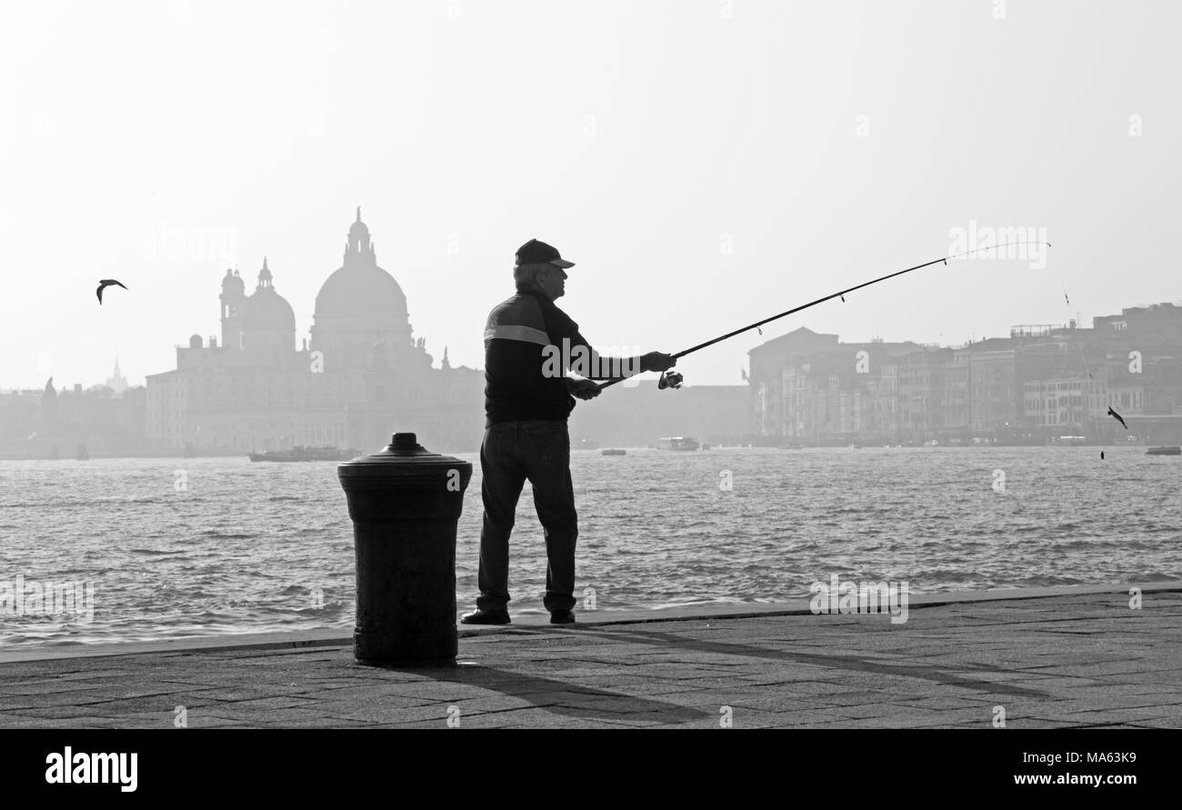 Venezia, Italia - 14 Marzo 2014: pescatore da Riva San Biagio waterfront e silhouette di Santa Maria della Salute chiesa. Foto Stock