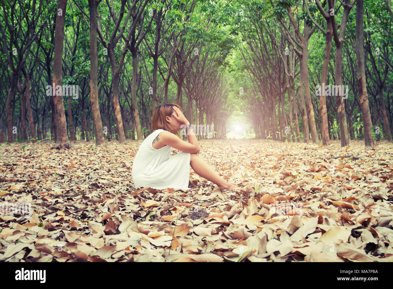Triste donna Hands off il suo volto così tristemente seduto su foglia secca nella foresta Foto Stock