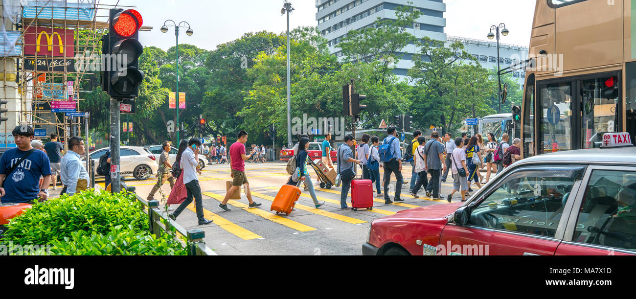 KOWLOON, HONG KONG - 18 settembre 2017; tipicamente Asian downtown city street scene i viaggiatori con le valigie incrocio a luce rossa Foto Stock