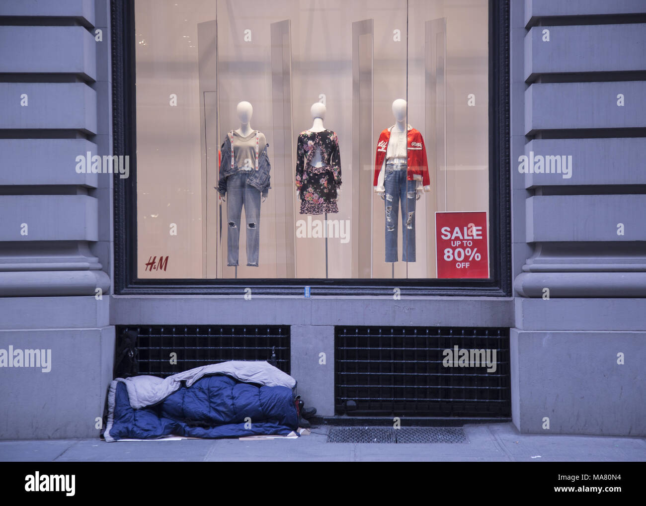 Traversina senzatetto nella parte anteriore di un H&M negozio finestra di visualizzazione nel quartiere di Chelsea di Manhattan NYC. Foto Stock