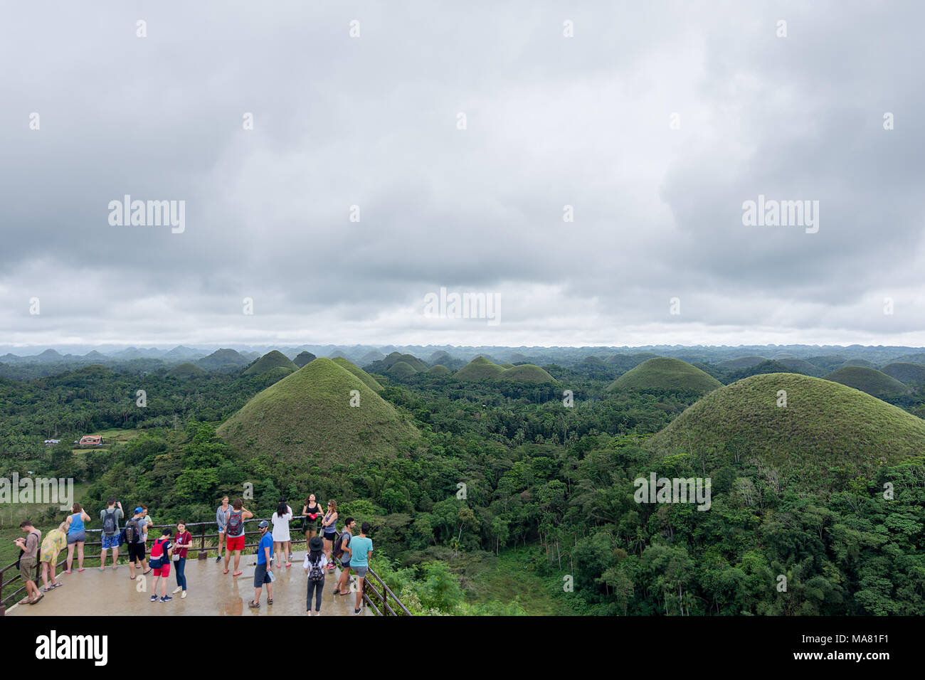 Un gruppo di giovani di sesso maschile e femminile ai turisti in piedi sulla piattaforma di osservazione guardando oltre il famoso cioccolato colline landmark in Bohol provincia del P Foto Stock