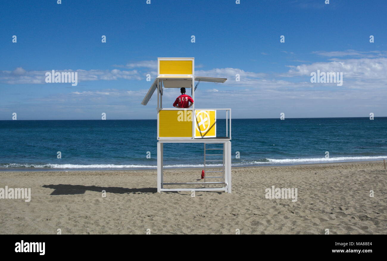 Un bagnino si affaccia al mare dalla sua cabina su una spiaggia deserta. Foto Stock