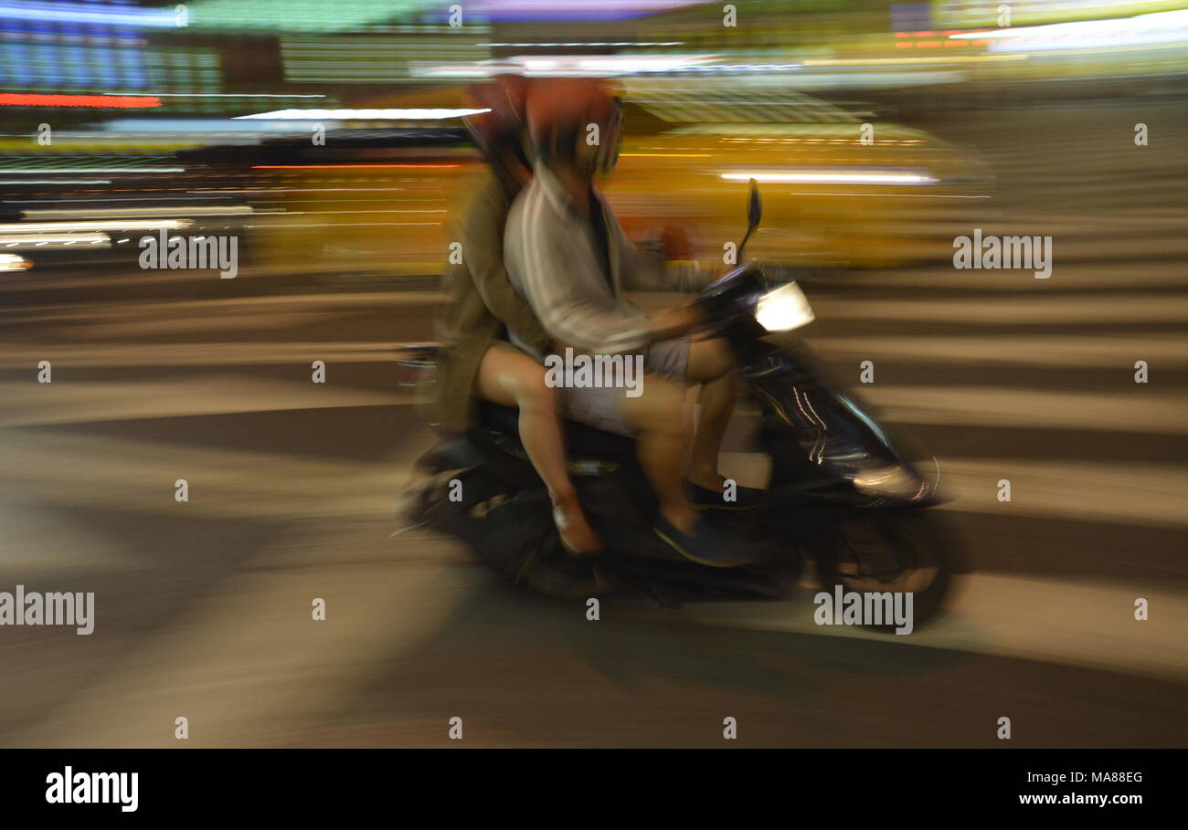Due giovani su uno scooter racing attraverso una città di notte Foto Stock