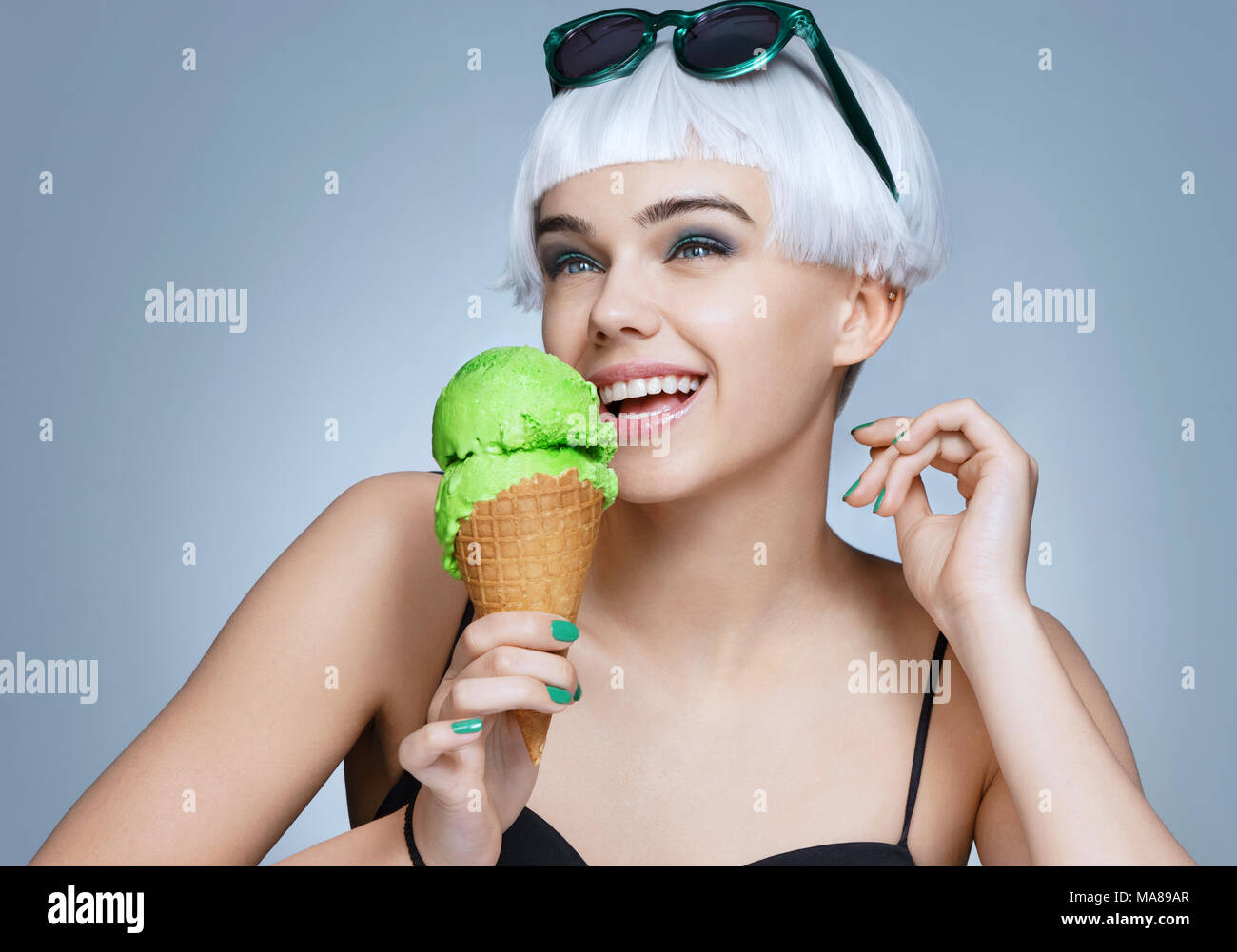 Felice moda ragazza godendo il pistacchio gelati su sfondo blu. Stile di vita felice Foto Stock