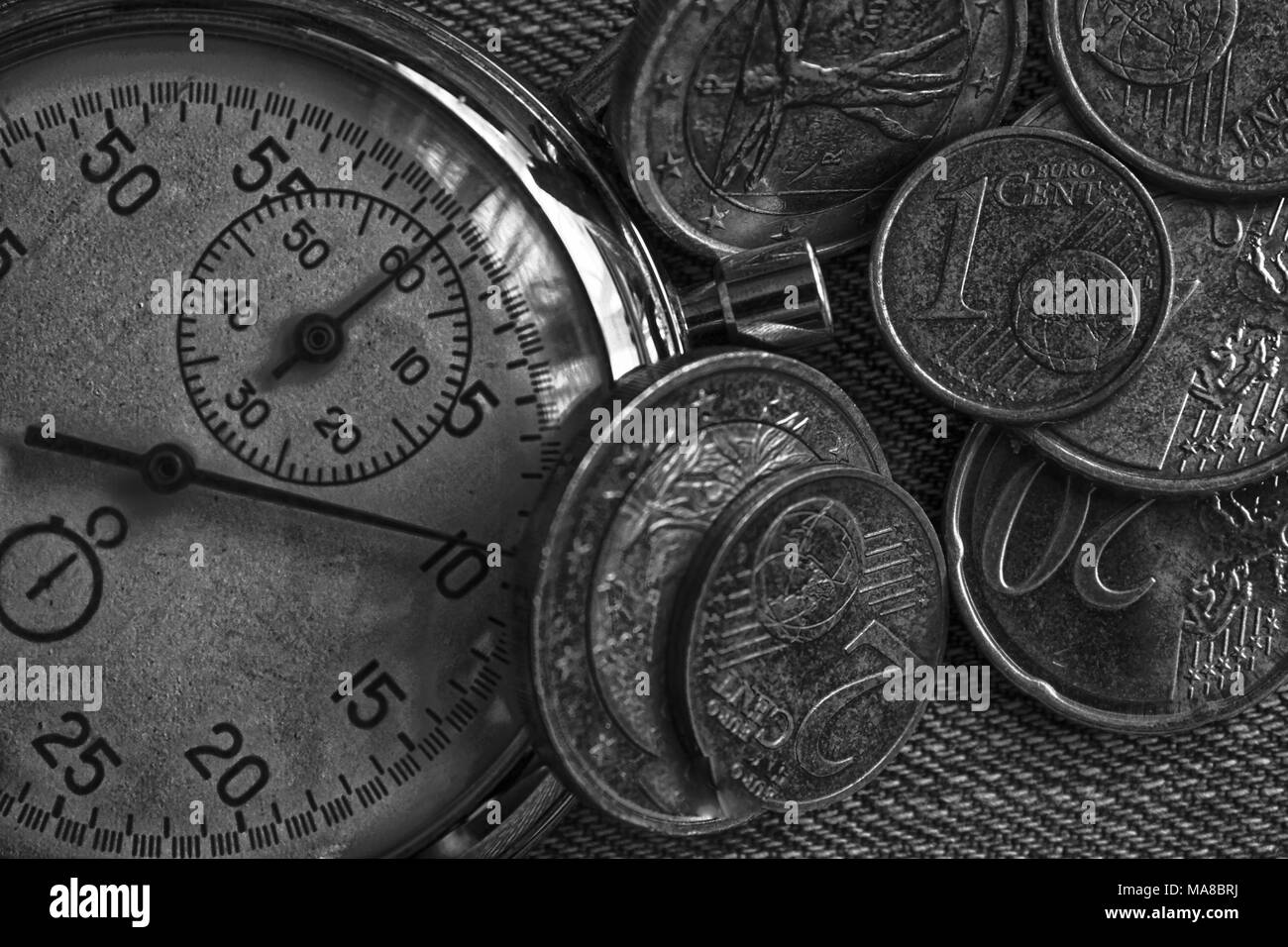Pila di monete in euro con il vecchio vintage cronometro sul vecchio usurato jeans sfondo. Foto Stock