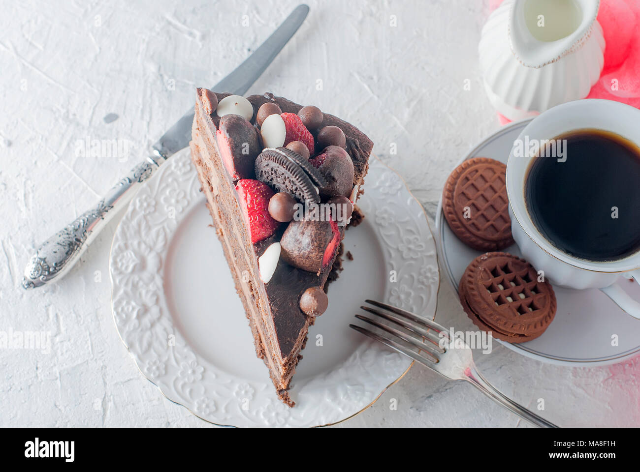 Pezzo di torta al cioccolato sulla piastra bianca, una tazza di caffè nero,  brocca e biscotti al cioccolato su sfondo bianco. Vista superiore, copia  dello spazio Foto stock - Alamy