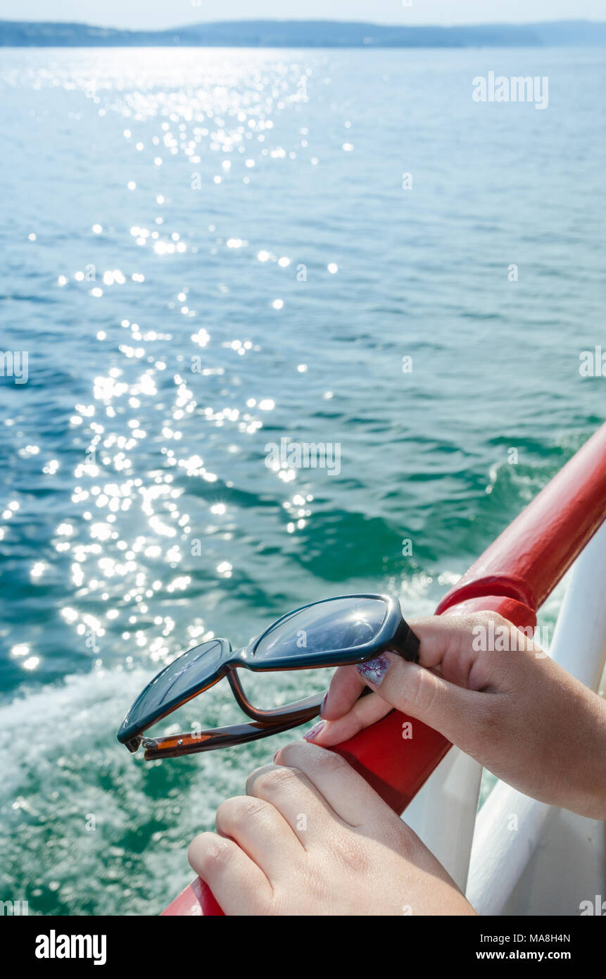 Le mani del turista femminile viaggiare per mare traghetti e ai piedi della rampa, tenendo i suoi occhiali da sole con un'isola essendo visibile all'orizzonte superiore Foto Stock