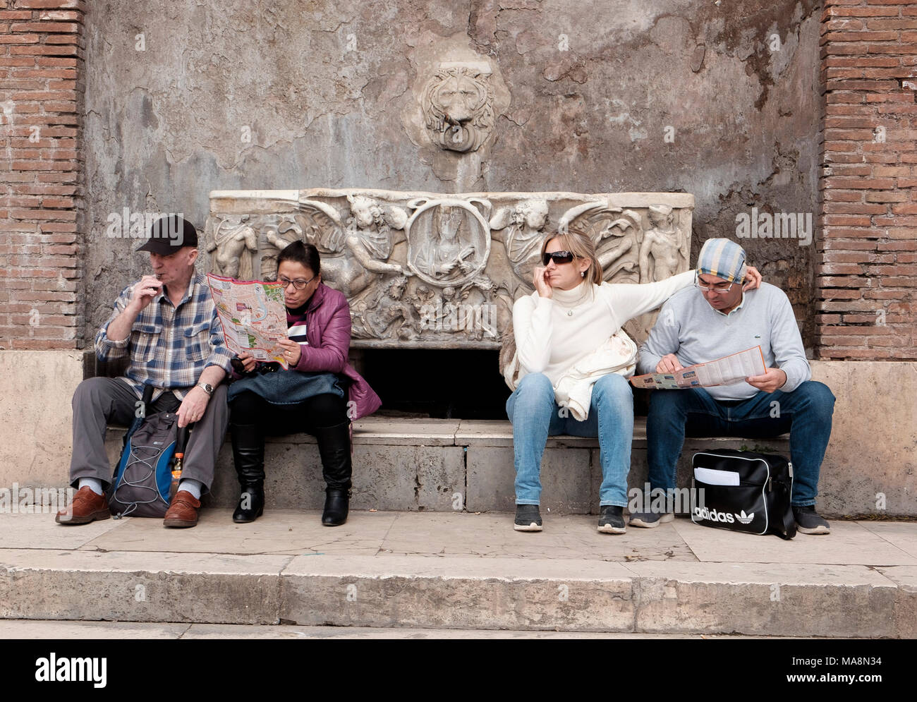 I turisti seduti su una pietra ornata panca su Via dei Fori Imperiali vicino al Colosseo, Roma mappe di consulenza Foto Stock