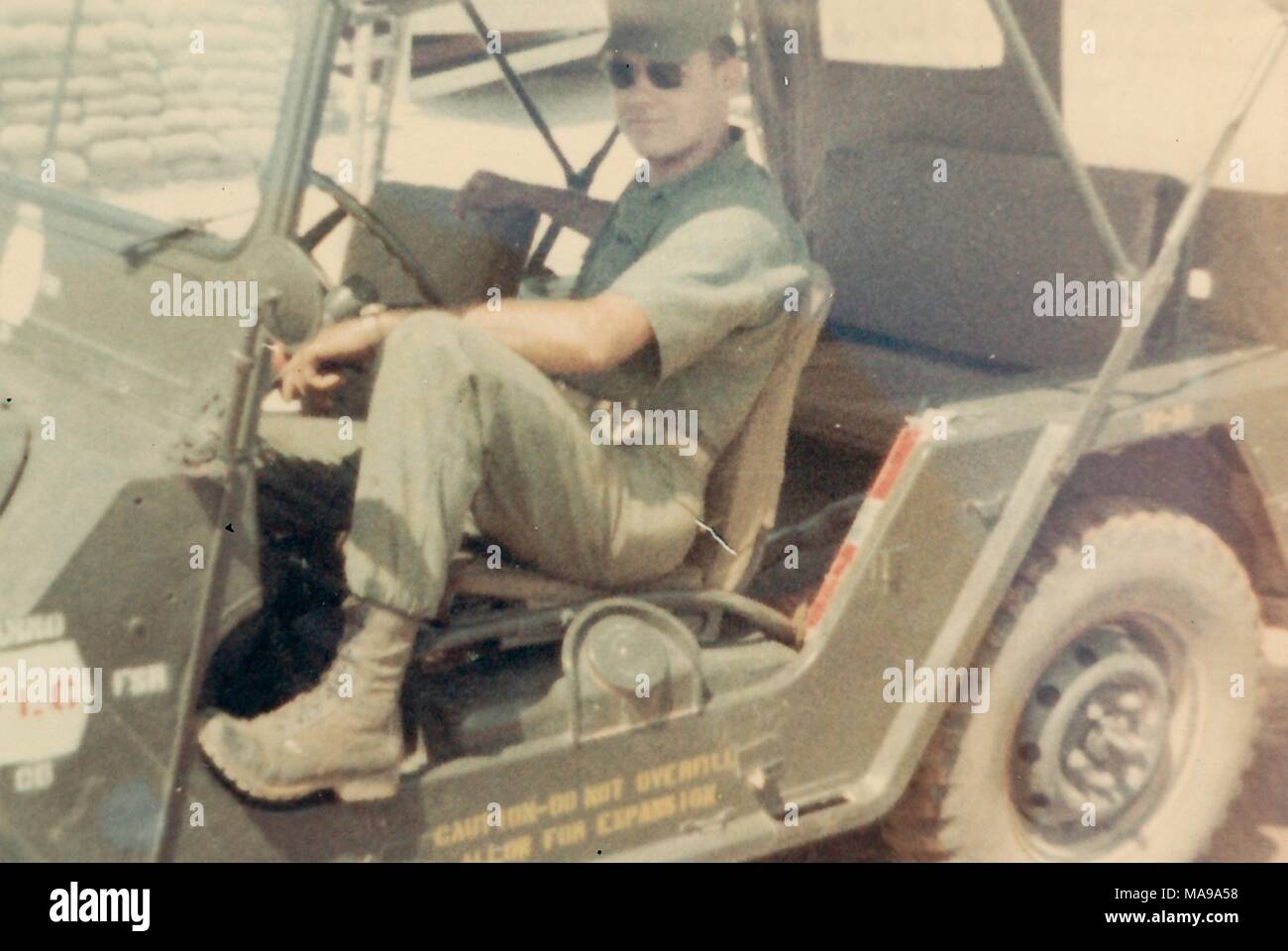 Fotografia a colori, di un soldato di sesso maschile, in full-length, tre quarti, vista di profilo, che indossa una uniforme, occhiali da sole e cappello, guardando la telecamera con un espressione rilassata sul suo volto, mentre sedendo nel sedile del conducente di un open-sided jeep, fotografato in Vietnam durante la Guerra del Vietnam (1955-1975), 1968. () Foto Stock