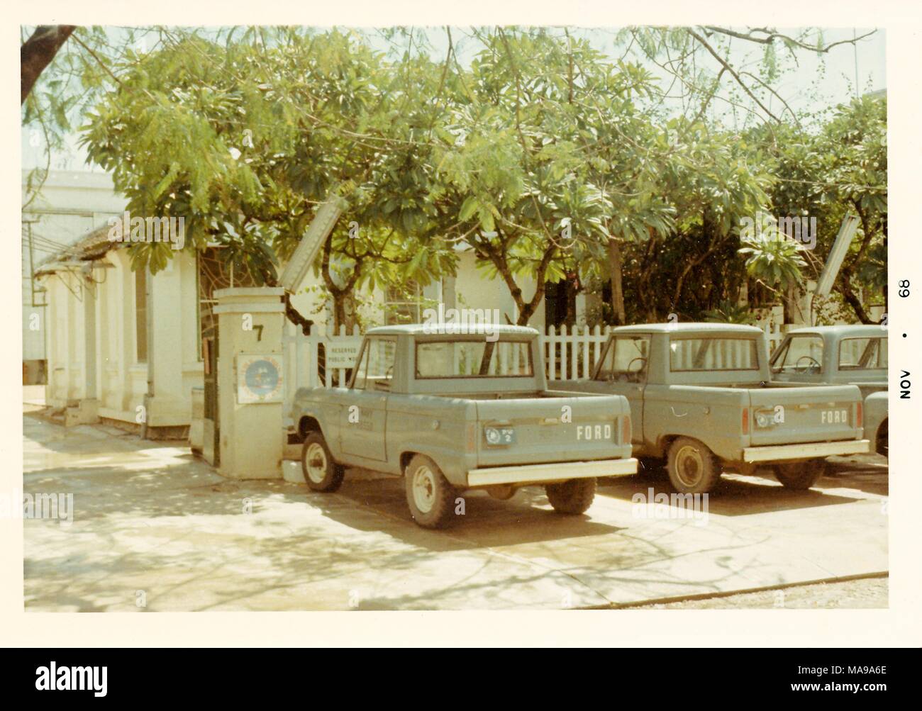 Fotografia a colori che mostra tre pickup Ford camion parcheggiato di fronte a Picket Fence, con alberi e una casa bianca sullo sfondo, fotografato in Vietnam durante la Guerra del Vietnam (1955-1975), 1968. () Foto Stock