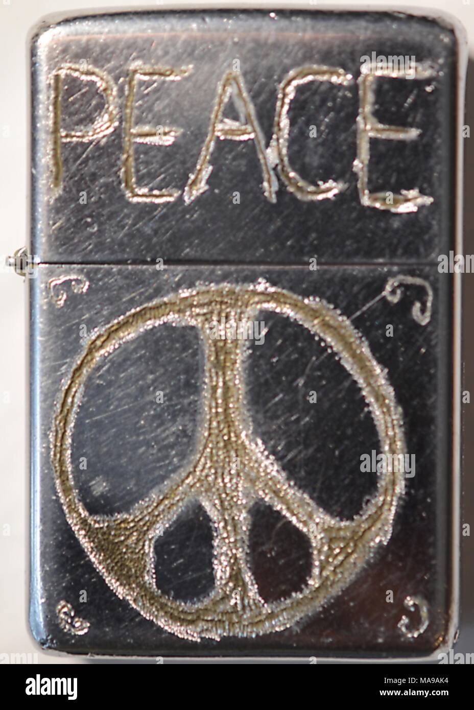 Close-up di metallo mostra Zippo accendino su cui il proprietario ha inciso a mano il simbolismo hippie comprendenti la parola pace e un simbolo di pace, 1968. () Foto Stock