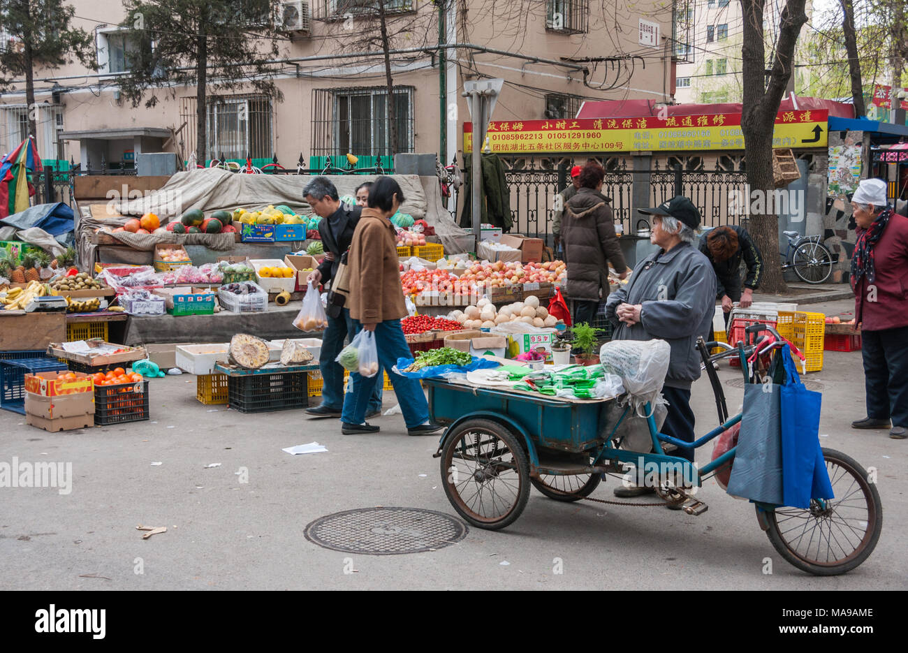 Pechino, Cina - 26 Aprile 2010: il mercato pubblico scenario dove vecchia donna vende il sedano e verde sacchetti ripiegati disattivata blu triciclo. Altre verdure e frutta di un Foto Stock