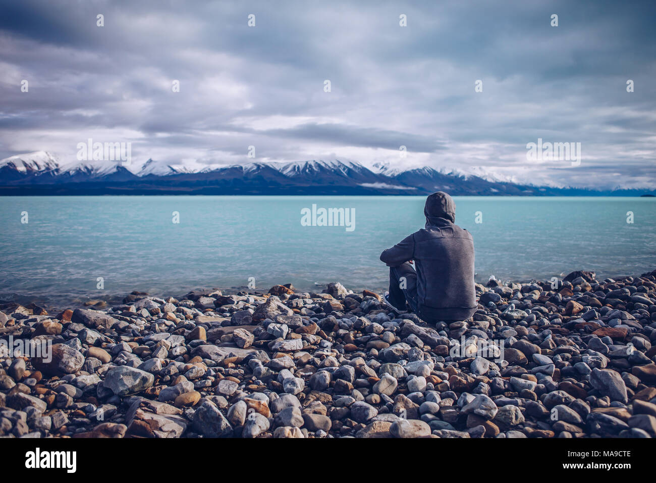 Giovane uomo che guarda sul Lago Tekapo e delle montagne innevate in Nuova Zelanda Foto Stock