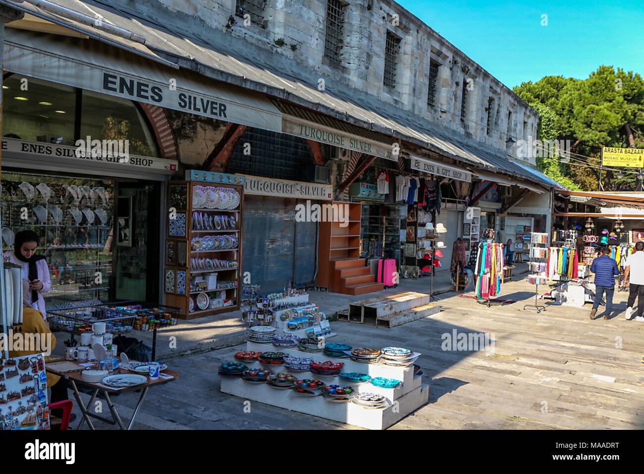 Vista di persone camminare nei pressi di numerose vetrine riempito con colorati souvenir, incluse ceramiche, sciarpe e gioielli in argento, situato nell'Arasta Bazaar nel quartiere di Sultanahmet di Istanbul, Turchia, 10 novembre 2017. () Foto Stock