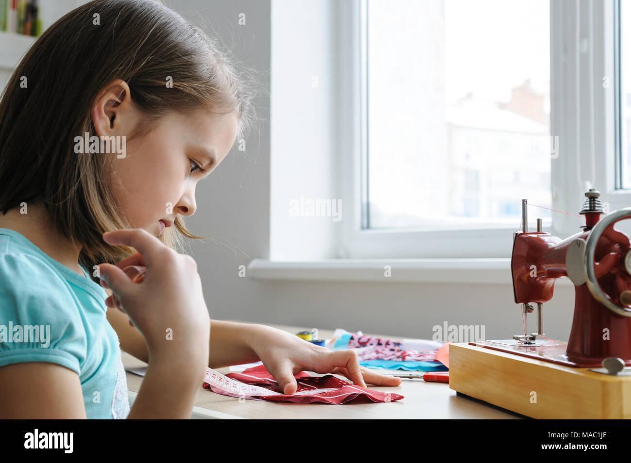 La ragazza è cucito un abito per una bambola . Ella utilizzando un nastro di misurazione per misurare il prodotto. Foto Stock