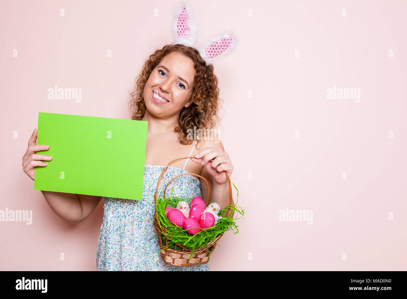 Bella donna tenere decorazioni di pasqua e poster in bianco con orecchie di coniglietto rosa su sfondo colorato con copia spazio. Foto Stock