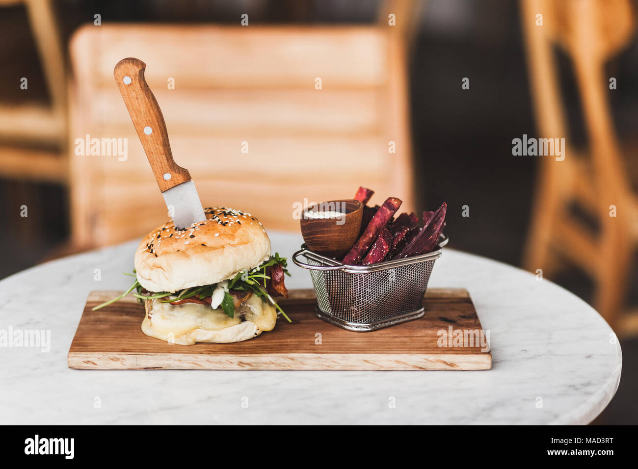 Freschi e saporiti burger con coltello all'interno con la salsa e fritto viola la patata dolce sul lato. Su bianco tavola rotonda sulla tavola di legno Foto Stock