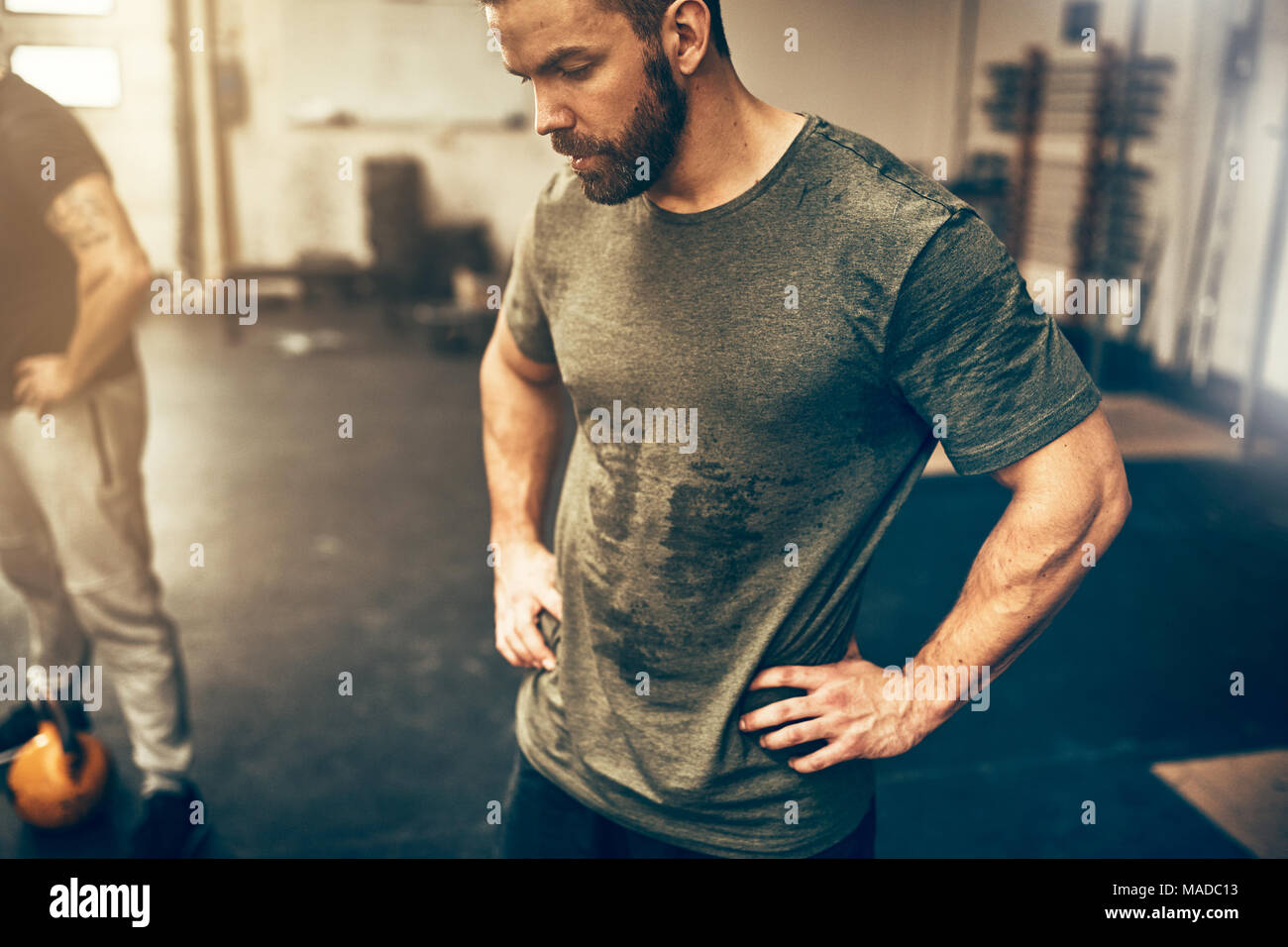 Montare il giovane uomo abbigliamento sportivo in piedi con le mani sui suoi fianchi in una palestra sudorazione dopo una sessione di allenamento Foto Stock