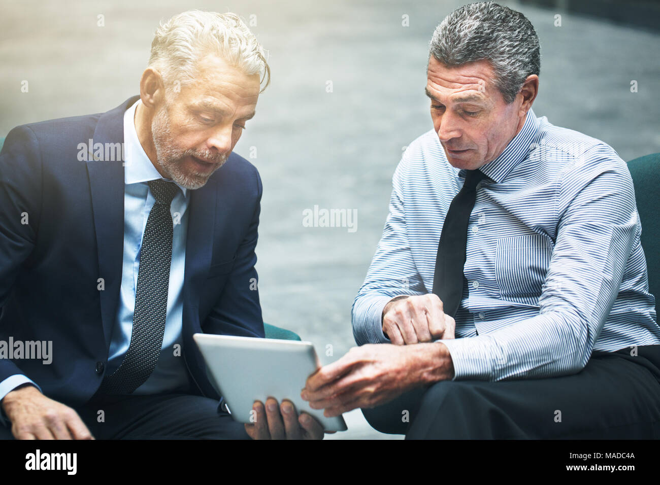 Due ben vestiti business maturi colleghi seduti su sedie in un ufficio lobby e parlare insieme e utilizzando una tavoletta digitale Foto Stock