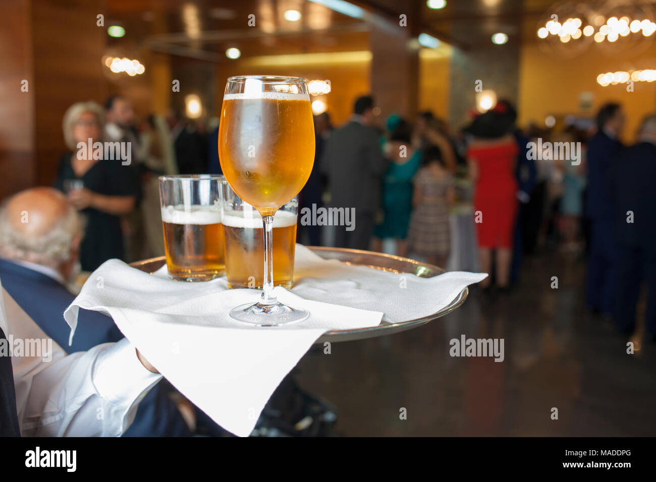 Le persone a bere birra al cocktail di benvenuto con abbigliamento formale. Cameriere tiene un vassoio con dei bicchieri e calice di vetro Foto Stock