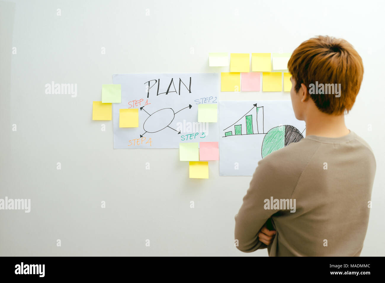 Giovane uomo asiatico si erge di fronte al suo piano finanziario in camera Foto Stock