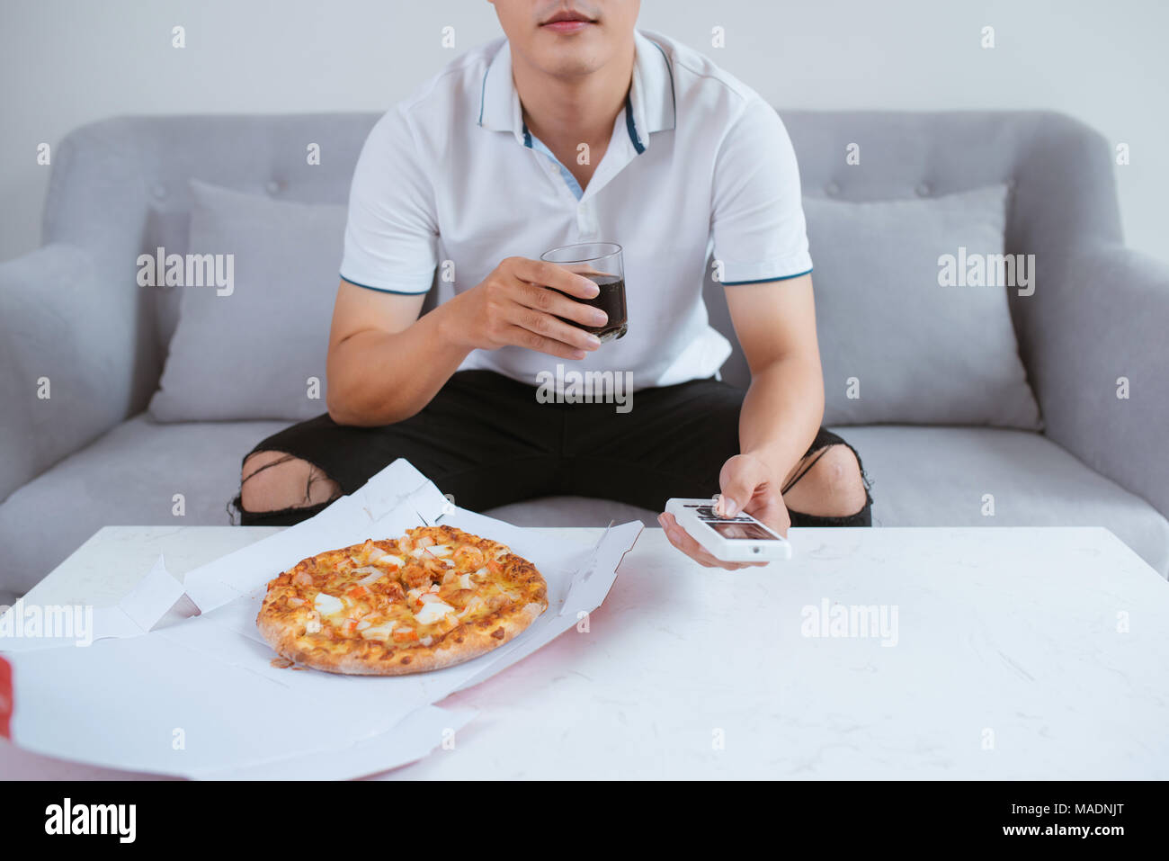 Uomo di guardare la TV e mangiare la pizza con soft drink. Close up. Seduto sul divano Foto Stock