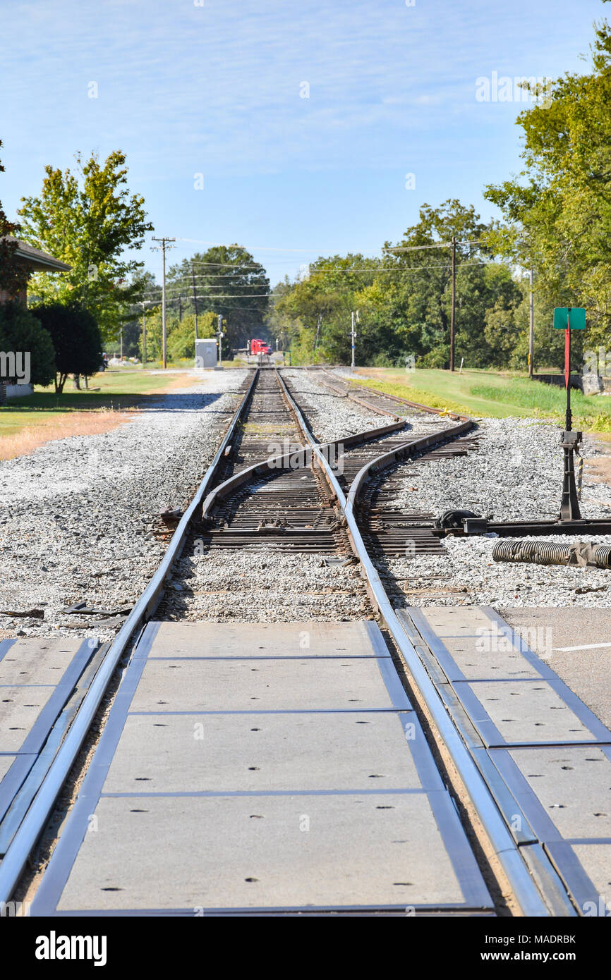 Trasferimento della ferrovia nei pressi di attraversamento stradale con alberi e cielo blu Foto Stock
