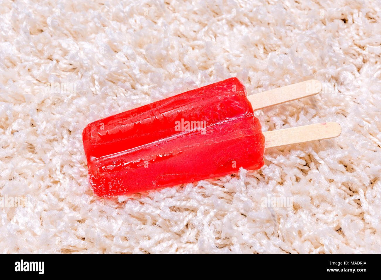 Un lasso di tempo di una fusione di ghiaccioli sul tappeto bianco mostra il gelido trattare la massa fusa in un succo appiccicoso e assorbire destra in moquette. Foto Stock