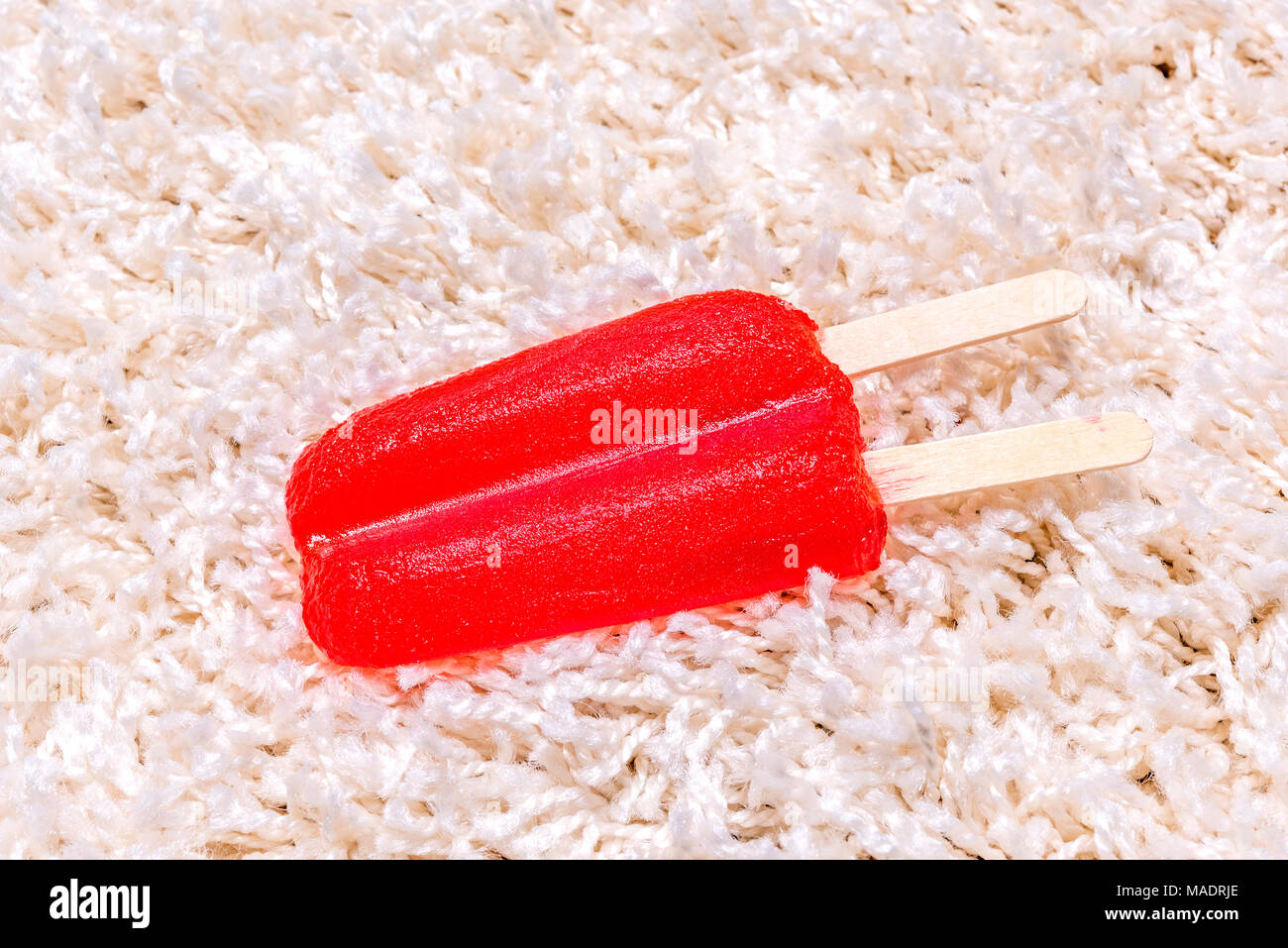 Un lasso di tempo di una fusione di ghiaccioli sul tappeto bianco mostra il gelido trattare la massa fusa in un succo appiccicoso e assorbire destra in moquette. Foto Stock