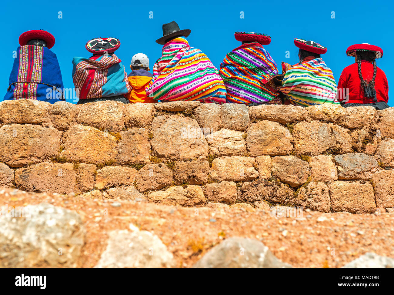 Un gruppo di indigeni Quechua donne e un ragazzo in chat su un antico muro Inca nel sito archeologico di Chincheros vicino alla città di Cusco, Perù. Foto Stock