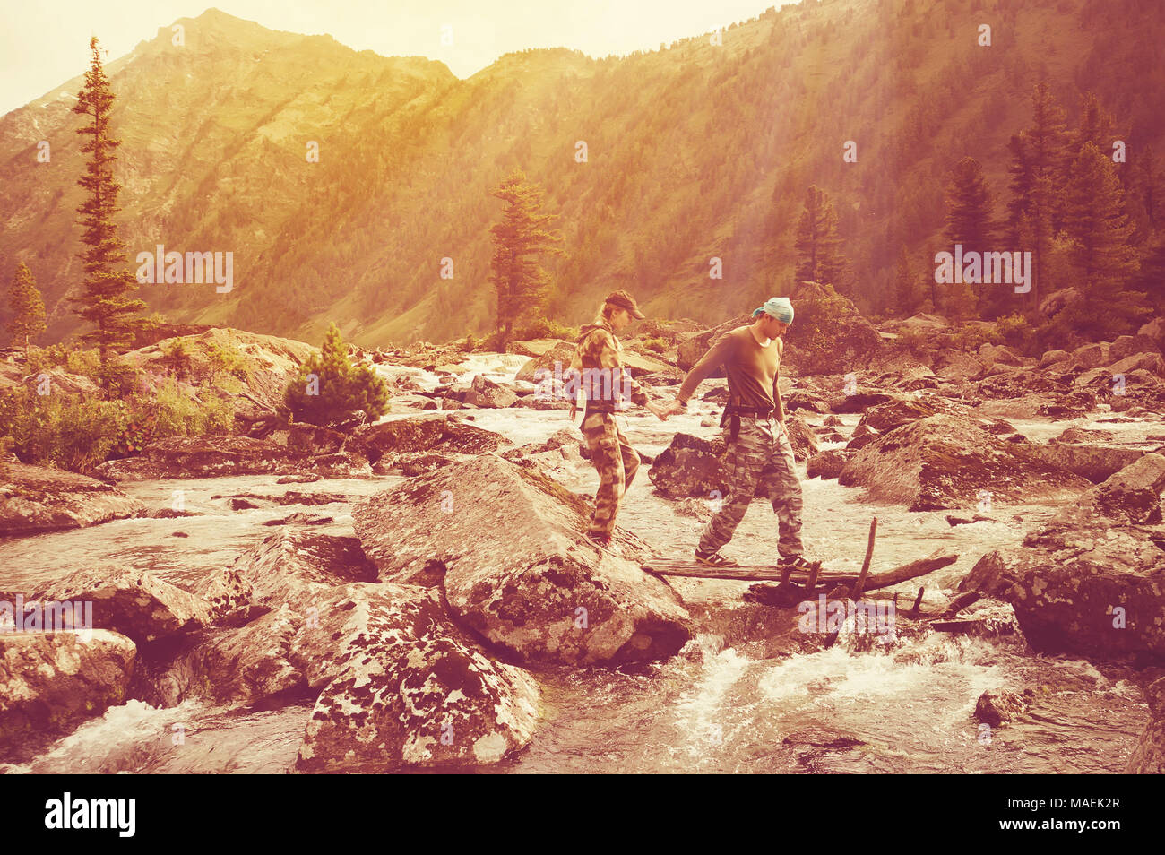 I turisti ragazzo e ragazza andare oltre il fiume di montagna tenendo le mani. Foto Stock